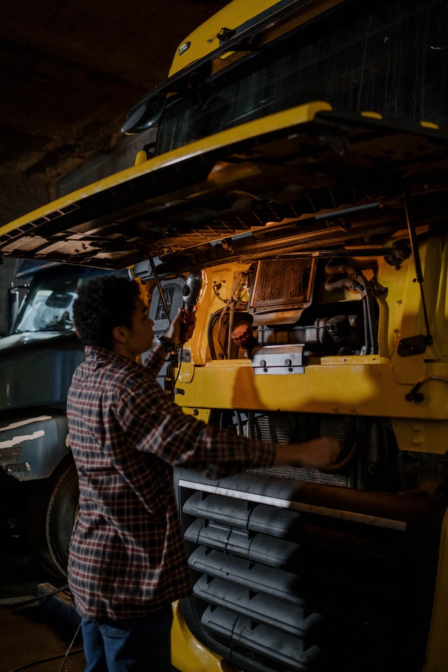 pexels-cottonbro-studio-7541351 A person repairing a yellow truck engine in a dark garage